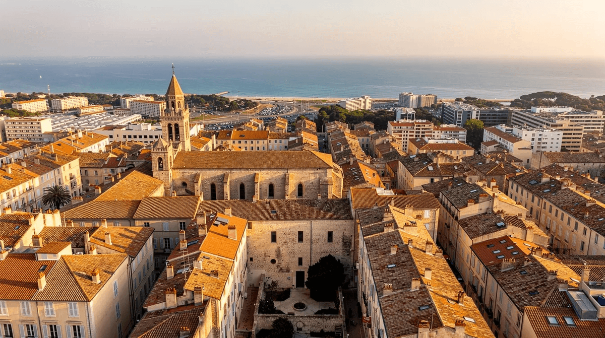 Vue aérienne de Montpellier mettant en avant les toits de l'Écusson, avec la mer Méditerranée scintillant à l'horizon. Cette image offre un aperçu de la ville, idéale pour ceux qui envisagent une location de voiture à Montpellier pour explorer les attractions locales.