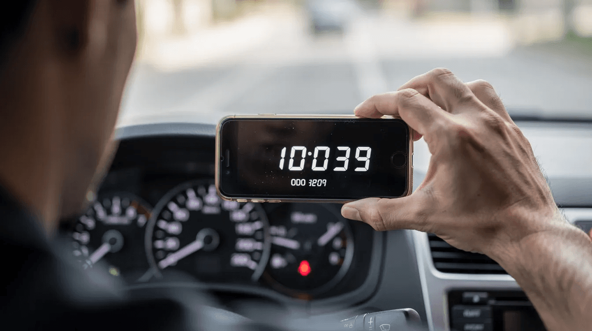 Une personne prend en photo le compteur kilométrique d'une voiture de location, mettant en avant le kilométrage parcouru lors d'un road trip. Cette image illustre l'importance de suivre le kilométrage illimité pour optimiser les voyages en véhicule.