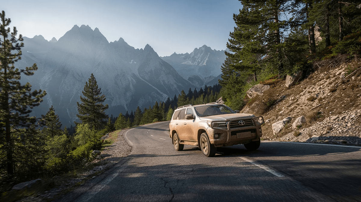 Un 4x4 élégant roule sur une route de montagne sinueuse, entouré de paysages verdoyants de forêt et de crêtes majestueuses en arrière-plan. Ce véhicule tout terrain offre une aventure parfaite pour explorer les régions montagneuses de France.
