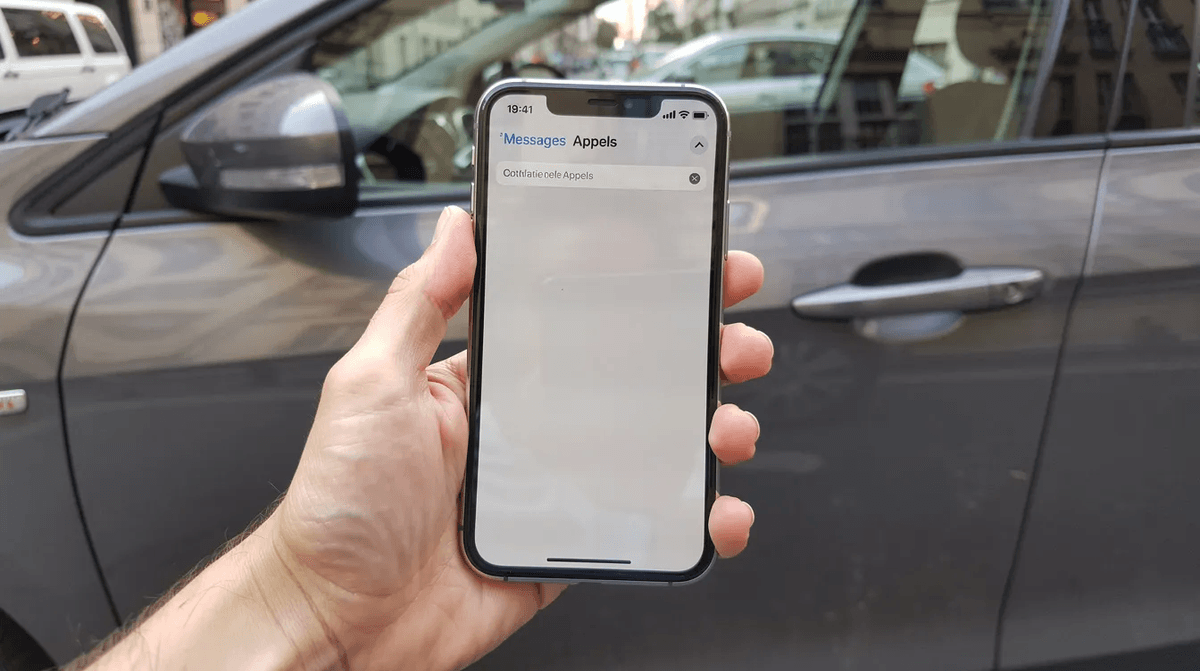 Une main tient un smartphone, affichant une application de location de voiture, devant la portière d'un véhicule garé en ville. Cette image illustre l'utilisation de services comme Getaround pour louer une voiture facilement.