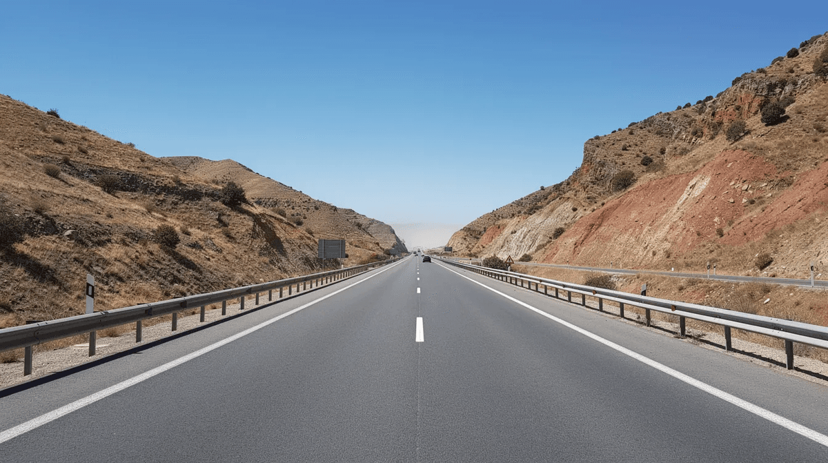 Une autoroute espagnole à deux voies s'étend à travers un paysage montagneux aride, baignée par un soleil éclatant. Cette image évoque la liberté de voyager en voiture en Espagne, idéale pour ceux qui souhaitent louer une voiture pour explorer les magnifiques paysages du pays.