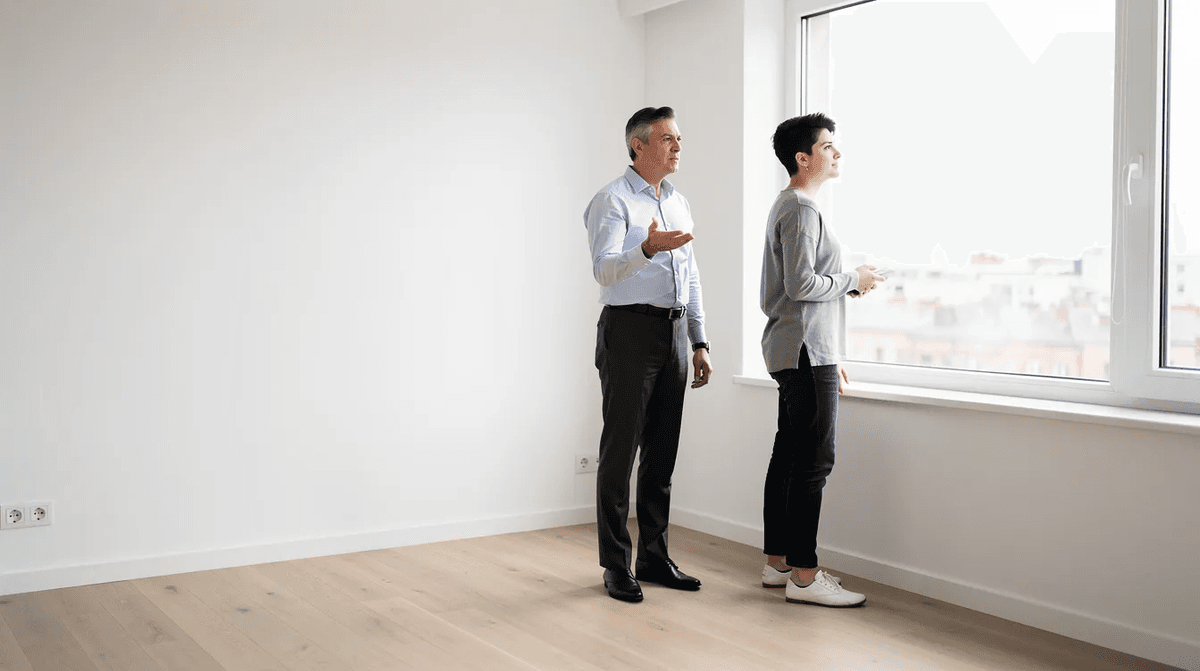 Une jeune personne explore un appartement vide en compagnie d'un agent immobilier, admirant la lumière qui entre par la fenêtre d'une chambre spacieuse. Ce moment de recherche de logement pourrait représenter une opportunité pour un futur colocataire dans une ville comme Paris ou Lyon.