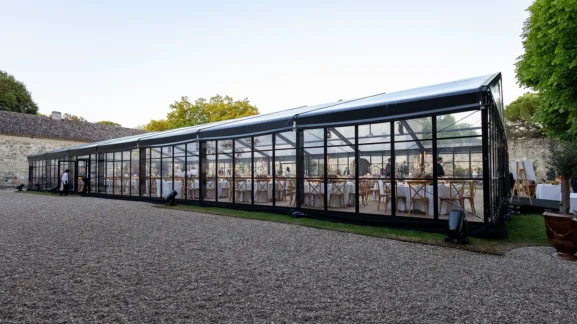Location materiel evenementiel : grande tente transparente élégante installée en extérieur pour réception avec tables dressées et invités